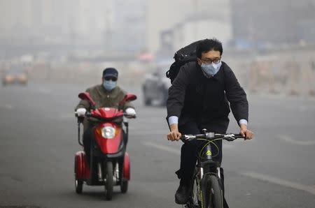 Residents wearing masks travel on a bicycle (R) and an electric tricycle along a street on a hazy day in Beijing, October 9, 2014. REUTERS/Barry Huang
