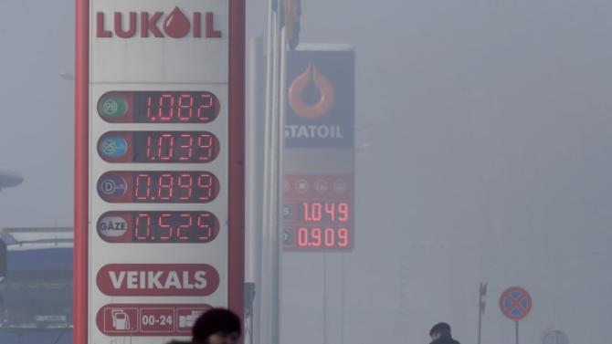 People walk past "Lukoil" and "Statoil" fuel stations displaying prices 1,125 USD and 1,136 USD per litre of basic unleaded petrol during a foggy winter day in Limbazi
