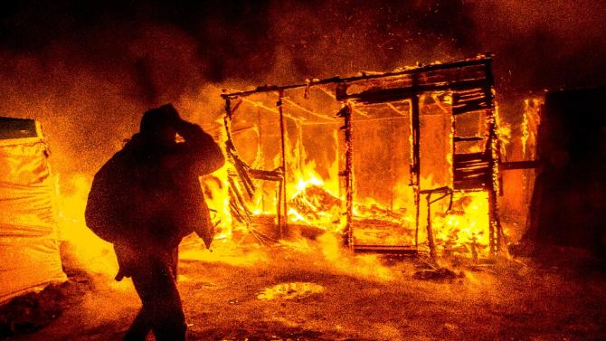 A migrant walks past burning shacks, in the "Jungle" migrant camp, as half of the camp is being dismantled, in Calais on March 1, 2016