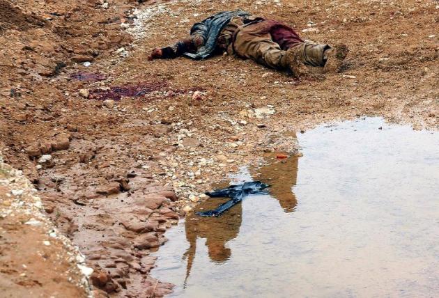 Un supuesto combatiente del grupo Estado Islámico yace muerto ante dos milicianos kurdos cuyas figuras se reflejan en un charco, el pasado 18 de diciembre en la ciudad de Zumar, al norte de Irak