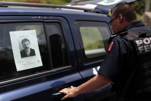 Un policía federal, junto a uno de los coches del cuerpo con una fotografía del narcotraficante fugitivo Joaquín &amp;quot;El Chapo&amp;quot; Guzmán en una carretera entre Ciudad de México y Acapulco el 14 de julio de 2015 (AFP | Pedro PARDO)