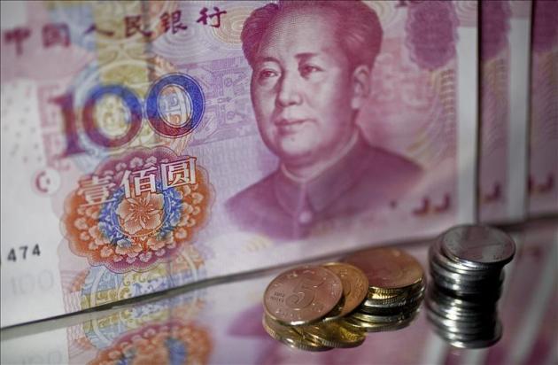Un billete de 100 yuan chinos pr Renminbi (RMB) junto a dos montones de monedas, en Pekín (China). EFE/Archivo