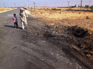 ARCHIVO - En esta foto de archivo del 20 de noviembre de 2013, un hombre y un niño pasan junto al cráter que dejó un coche bomba en el camino entre Rafá y el-Arish, Egipto. Las autoridades ordenaron a los residentes de la zona fronteriza con la Franja de Gaza el 28 de octubre de 2014 que abandonen sus hogares. El ejército piensa demoler las viviendas e instalarse para combatir el tráfico de armas y personas entre Egipto y Gaza. (AP Foto/Ahmed Abu Deraa, File)