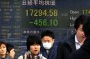 Des piétons passent devant des tableaux d'indices boursiers, le 3 février 2016 à Tokyo, au Japon