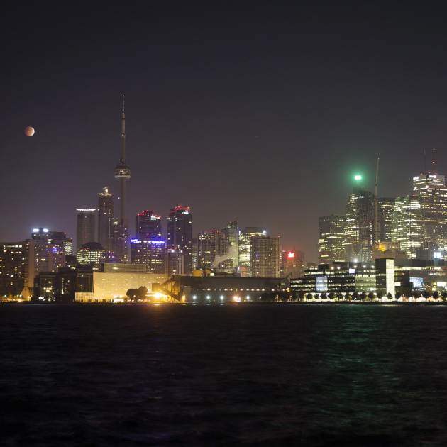 The moon turns orange during a total lunar eclipse behind the CN Tower and the skyline during moonset in Toronto
