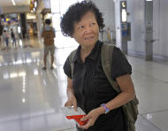 Mary Seow holds a boarding pass after she checked in with her son, in the background carrying a backpack, at the airport in Hong Kong, Saturday, Nov. 21, 2015. Seow, a Singaporean woman who went missing nearly five years ago, has been reunited with her son after her plight was reported in an Associated Press story about people who sleep at 24-hour McDonald's outlets in Hong Kong. (AP Photo/Vincent Yu)