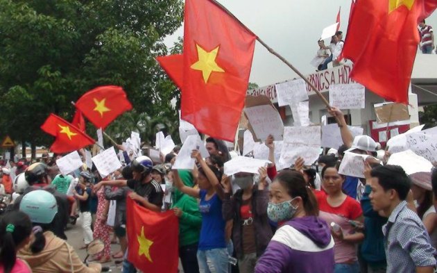 Protesters wave flags and hold placards on a street outside a factory building in Binh Duong on May 14, 2014