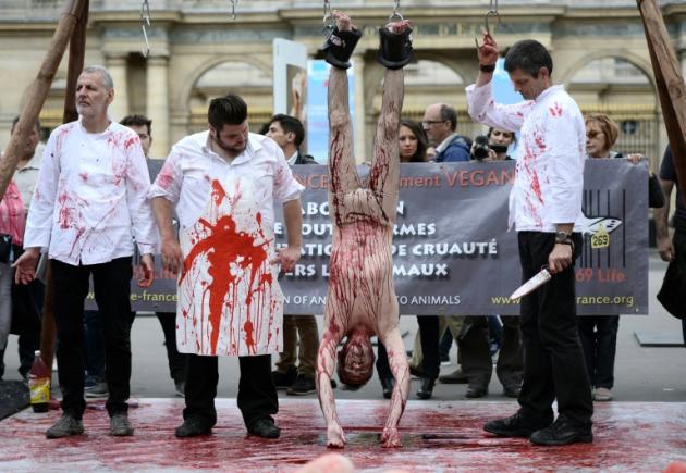 Un homme en slip, accroché par les pieds à des crocs de boucher avec, autour de lui, trois autres, en tablier de boucher, qui font mine de l'éviscérer, projetant des giclées de sang, un happening de militants de l'association "269 life"à Paris le 26 septembre 2015 contre l'exploitation animale