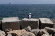 A migrant sits on a concrete block at the waterfront of the Sicilian harbour in Palermo April 19, 2015. REUTERS/Alessandro Bianchi TPX IMAGES OF THE DAY