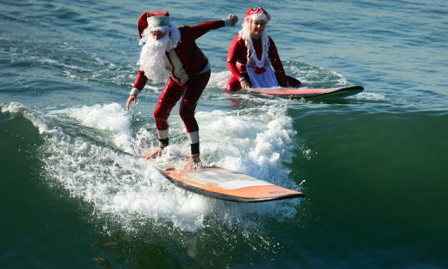Surfing Santa, Michael Pless, 62, (L) catches a wave as his wife Jill watches, at Seal Beach , south of Los Angeles, on December 21, 2012 in California. Pless, who runs a surfing school, has been dressing up as Santa Claus and taking to the waves in costume since the 1990s. AFP PHOTO / Frederic J. BROWNFrederic J. BROWN (Photo credit should read FREDERIC J. BROWN/AFP/Getty Images)