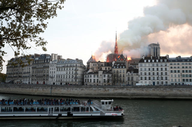 People watch from a tour boat on the River Seine as smoke billows and fire engulfs the spire of Notre Dame Cathedral in Paris, France April 15, 2019. REUTERS/Benoit Tessier
