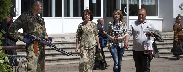 A gunman stands guard as local residents walk from a polling station in Slovyansk, eastern Ukraine, , May 11, 2014. (Alexander Zemlianichenko/AP)