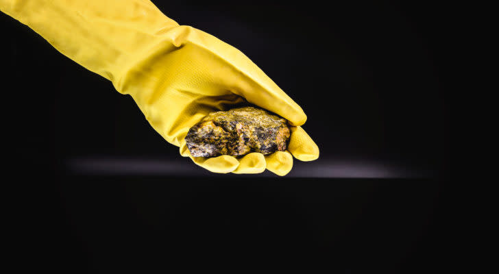 CCJ Stock: Hand in long yellow glove holding a chunk of uranium material